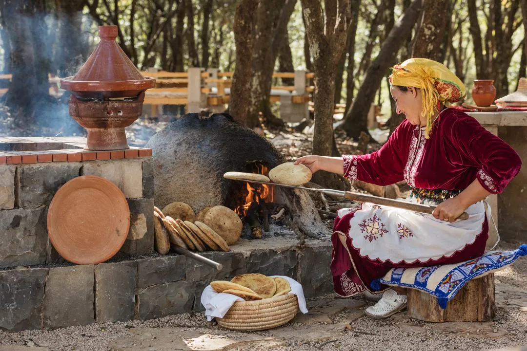 Une femme en tenue traditionnelle cuit des galettes sur un feu de bois en plein air