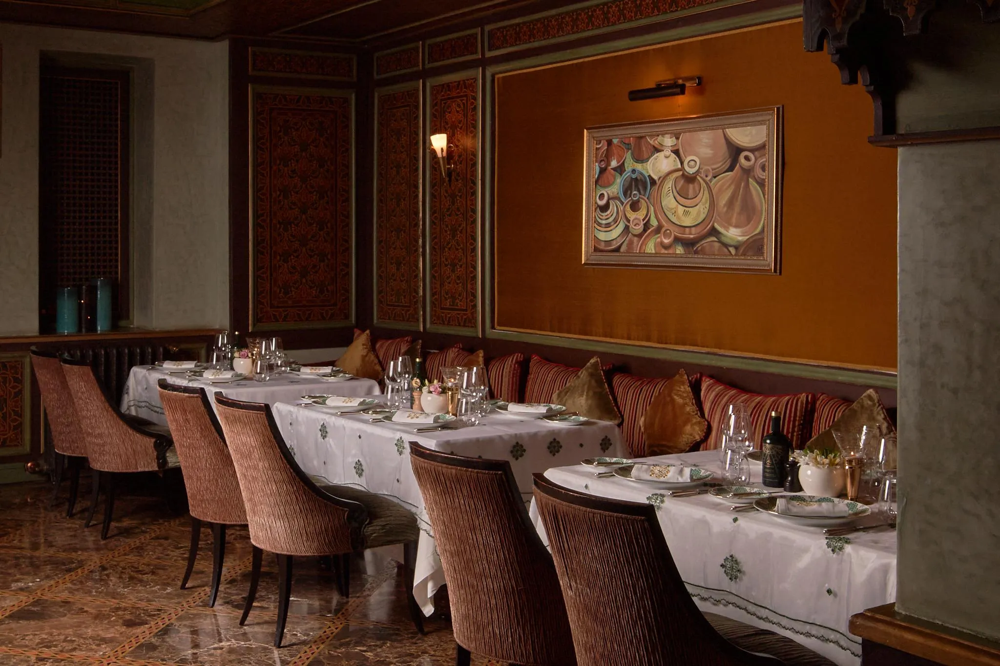 Une salle à manger élégante avec des tables dressées et des chaises rembourrées, décorée de coussins et d'un tableau mural coloré