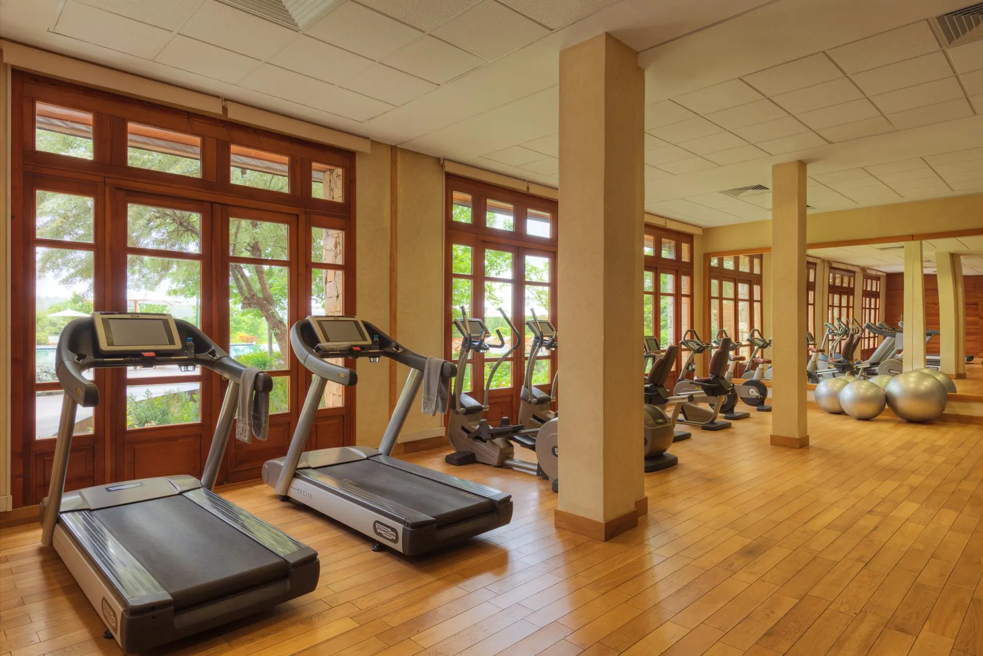 Salle de sport avec plusieurs tapis de course et vélos d'exercice devant de grandes fenêtres en bois