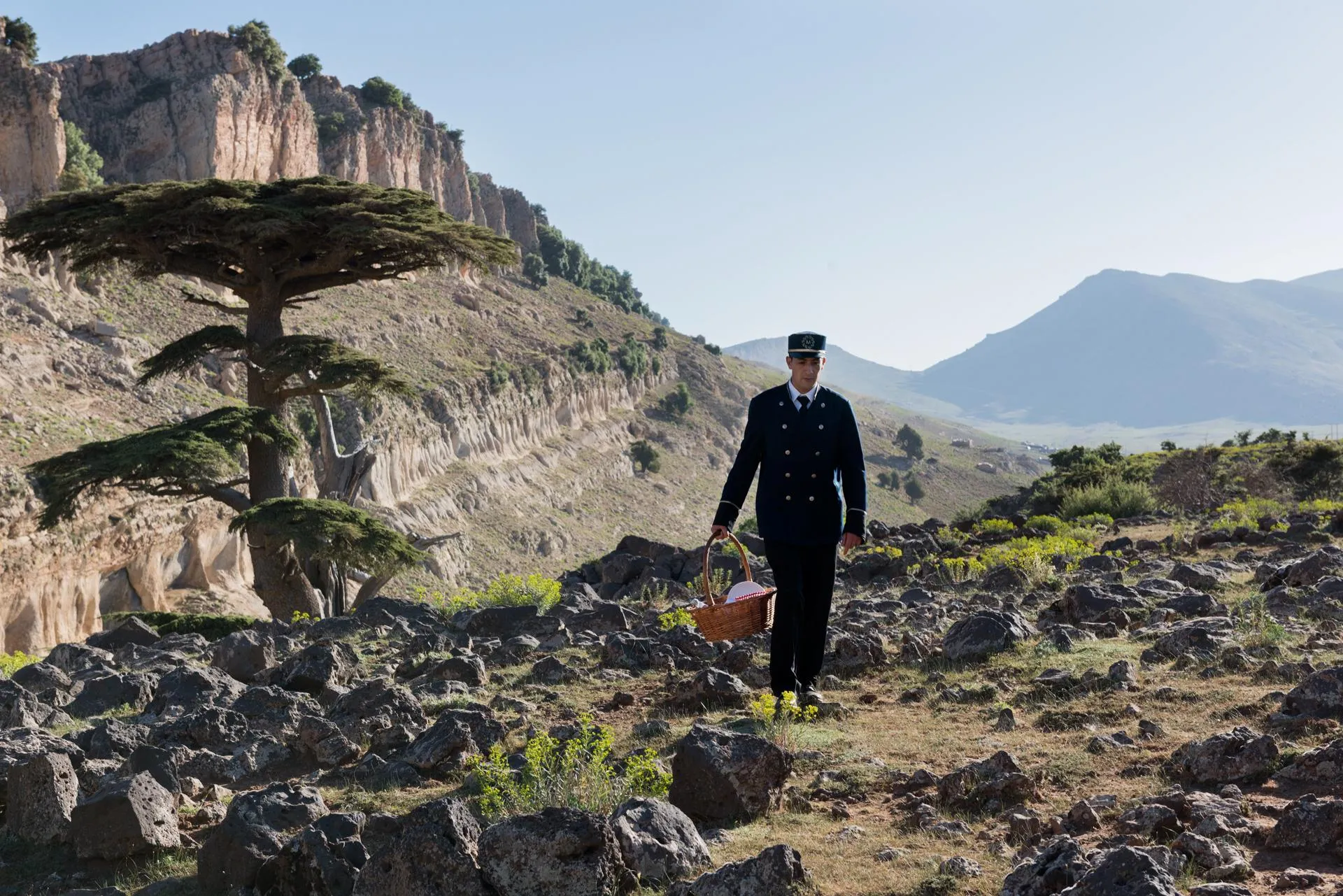 Un homme en uniforme marche dans un paysage montagneux rocheux en tenant un panier