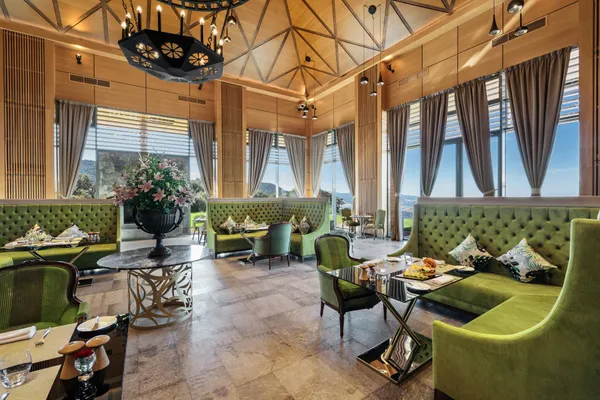 Un restaurant élégant avec des banquettes vertes, des tables dressées et de grandes fenêtres offrant une vue panoramique