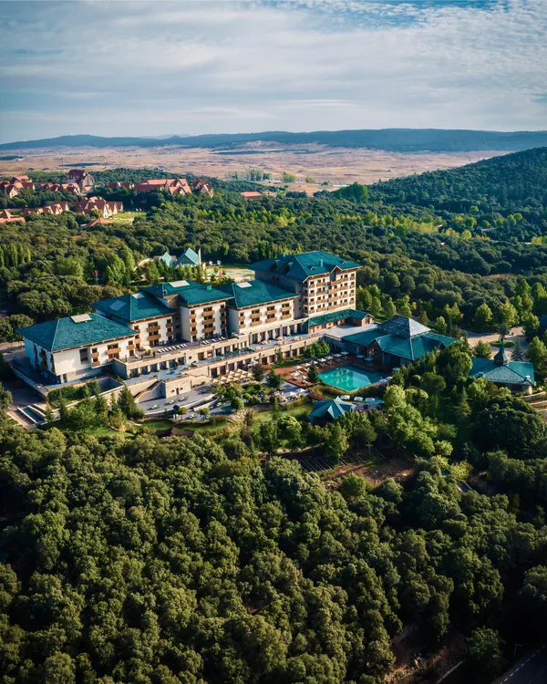 Un grand complexe hôtelier entouré d'une dense forêt avec des piscines et des bâtiments aux toits verts, vu depuis les airs
