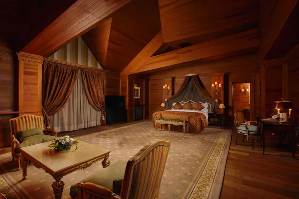 Chambre luxueuse en bois avec un grand lit à baldaquin, des canapés, une table et des lampes