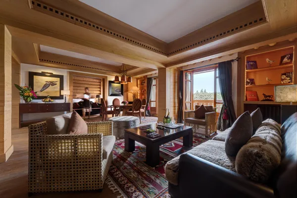Salon en bois avec canapés, fauteuils, table basse et vue sur l'extérieur par de grandes fenêtres