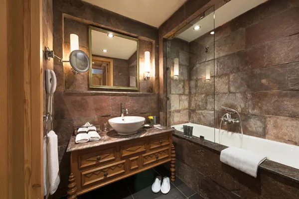 Salle de bain avec lavabo, miroir, baignoire et serviettes, murs en pierre et éclairage mural