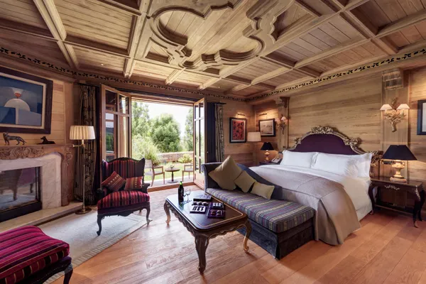 Chambre en bois avec lit, canapé, table basse, cheminée et portes-fenêtres ouvrant sur une terrasse extérieure