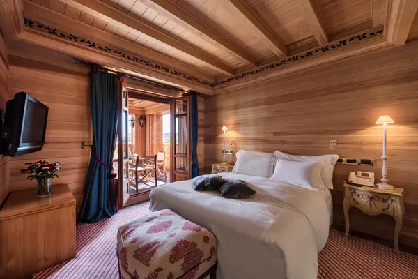 Chambre en bois avec un lit double, une télévision, une table de chevet avec une lampe et un téléphone, et une porte-fenêtre ouvrant sur un balcon