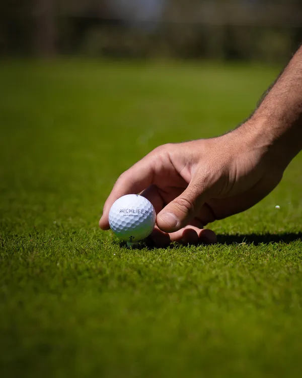 Une main place une balle de golf sur un tee sur un gazon vert