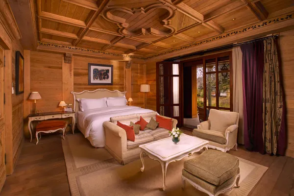 Chambre en bois avec lit double, canapé, fauteuils, table basse et fenêtres donnant sur l'extérieur