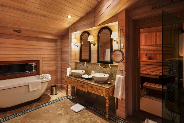 Salle de bain en bois avec baignoire, double vasque, miroir et porte ouverte sur un sauna