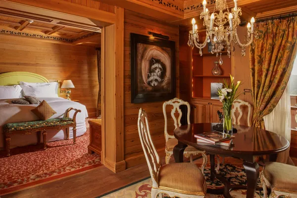 Chambre en bois avec lit, chandelier, tableau, table avec chaises et fleurs dans un vase