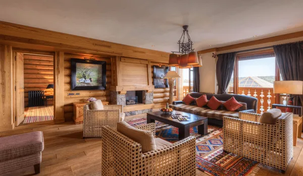 Salon en bois avec canapé, fauteuils en rotin, table basse, cheminée et grandes fenêtres